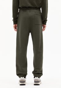 Groene joggingbroek met een elastische tailleband en boorden. Heeft een achterzak en een gladde, zachte textuur. G gedragen met grijze sneakers.