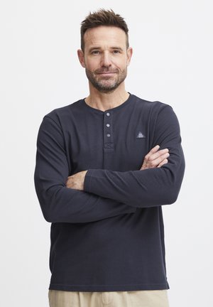 Marine langærmet henley skjorte med tre knapper ved kraven, tekstureret stof og et lille logo-patch på venstre bryst.