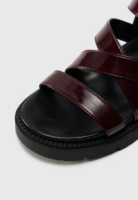 Sandales en cuir verni bourgogne avec trois larges sangles, semelle intérieure rembourrée noire et semelle en caoutchouc texturé pour une meilleure adhérence.