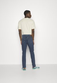 Jeans de mezclilla azul con un corte recto y diseño de cinco bolsillos, combinados con una camiseta de manga corta color crema y zapatillas verdes azules.