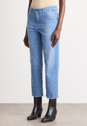 Lichtblauwe denim jeans met witte verticale stikpatronen, hoge taille, rechte pasvorm en een rafelige zoom, gecombineerd met zwarte enkelboots met hak.