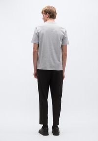 Trumpomis rankovėmis pilka marškinėliai su apvalia iškirpte, derinami su juodomis siaurėjančiomis kelnėmis ir tamsiais batais. Audinys atrodo minkštas, turintis vienalytę tekstūrą.