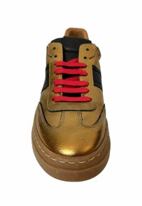 Goldfarbene Metallic-Sneaker mit schwarzen Streifen, leuchtend roten Schnürsenkeln und einer dicken braunen Sohle. Das Design zeichnet sich durch eine glatte Textur und Nähdetails aus.