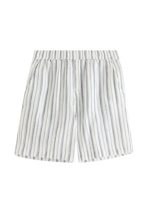 Teenager iført hvid t-shirt med korte ærmer og shorts med lodrette grå striber, hvide sokker og beige sneakers, står med hænderne i lommerne.