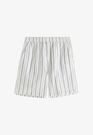 Teenager iført hvid t-shirt med korte ærmer og shorts med lodrette grå striber, hvide sokker og beige sneakers, står med hænderne i lommerne.