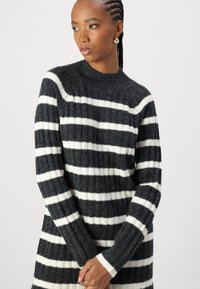 Pull rayé noir et blanc avec une texture côtelée, un col montant et des manches longues, présentant des rayures épaisses et fines en alternance.