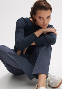 Marineblaues, geripptes Langarmoberteil kombiniert mit gemusterten marineblauen Hosen. Das Outfit hat eine taillierte Passform und wird durch weiße Sneaker ergänzt.