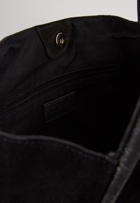 Svart tote-väska med en interiör i slät tygfoder och en läderetikett; har en magnetisk knappstängning och flera fickor för organisering.