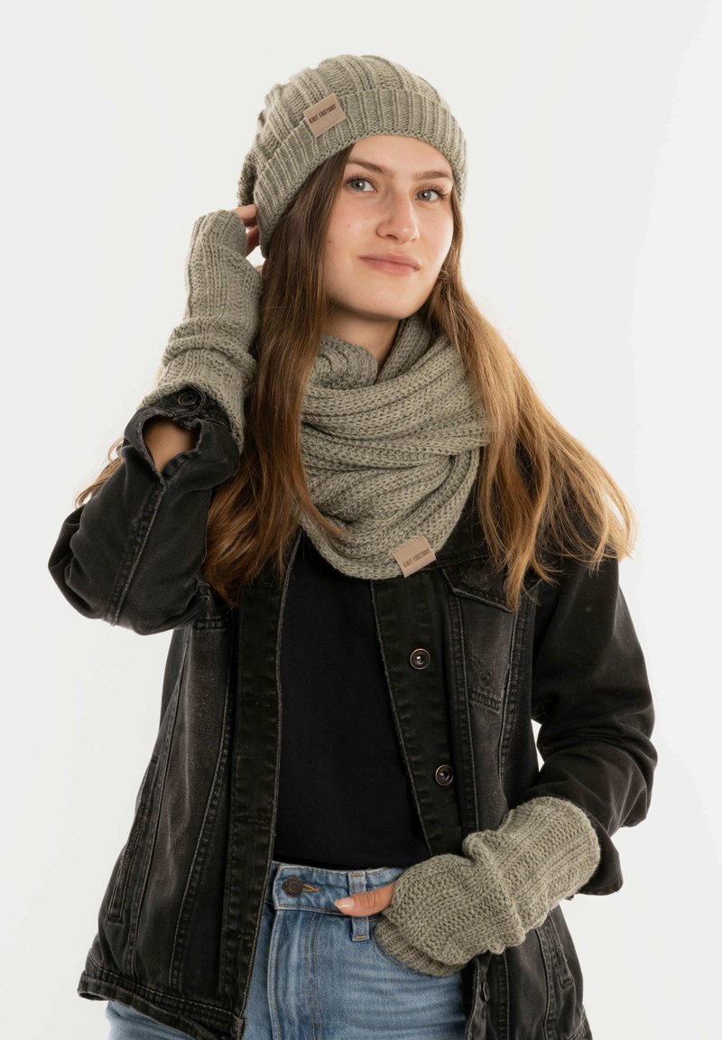 Gebreide olijfgroene beanie, sjaal en vingerloze handschoenen in een textuurpatroon; gedragen met een zwarte denimjas en een zwarte top.