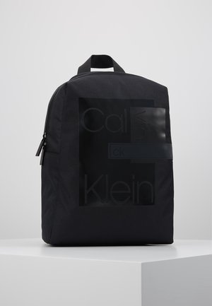 Black Calvin Klein backpack with subtle embossed logo on front, top handle, and double zipper closure, displayed on white surface.