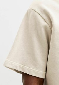 Posnetek v bližini bež kratkoročne bombažne srajce na temni koži na enostavni svetli podlagi.