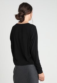 Svart långärmad topp med båtformad halsringning, gjord av mjukt material. Har en avslappnad passform och draperad rygg, tillsammans med en grå kjol.