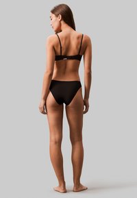 Set di bikini nero con spalline regolabili e chiusura a gancio. I pantaloni sono a vita alta, realizzati in tessuto morbido e dal design minimalista.