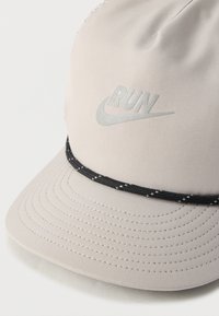 Γκρι σκουφί με στρογγυλεμένο στέμμα, μαύρη πλεξούδα και αντανακλαστικό λογότυπο με τη λέξη "RUN." Λεπτή υφή υφάσματος.