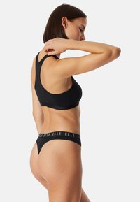 Zwarte katoenen sport beha met een racerback ontwerp, voorzien van een brede elastische band met de merknaam. Gecombineerd met bijpassende zwarte string onderbroek.