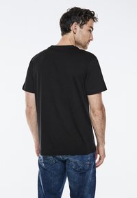 Sort bomulds T-shirt med klassisk rund hals, korte ærmer, løs pasform og glat tekstur, båret med blå denim jeans.
