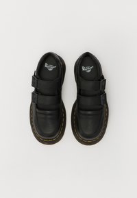 Schwarze Lederschuhe mit doppelten Klettverschlüssen, runder Spitze und gelben Nähten an der Sohle. Strukturiertes Material mit glatter Oberfläche.
