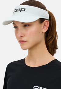 Weißer Sportvisier mit gebogenem Schirm, mit schwarzem "CEP"-Logo auf der Vorderseite. Glatte Stofftextur, kombiniert mit einem schwarzen Shirt.
