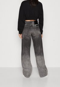 Högmidjade jeans med vida ben i en gradient från svart till grå denim. Har en bakfickdesign och en etikett på linningen.