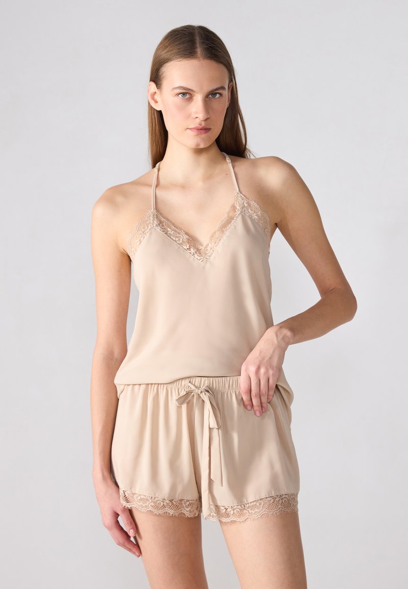 Beige satin cami med blondertrim og justerbare stropper, parret med matchende shorts med blonderdetaljer og snoreliv.