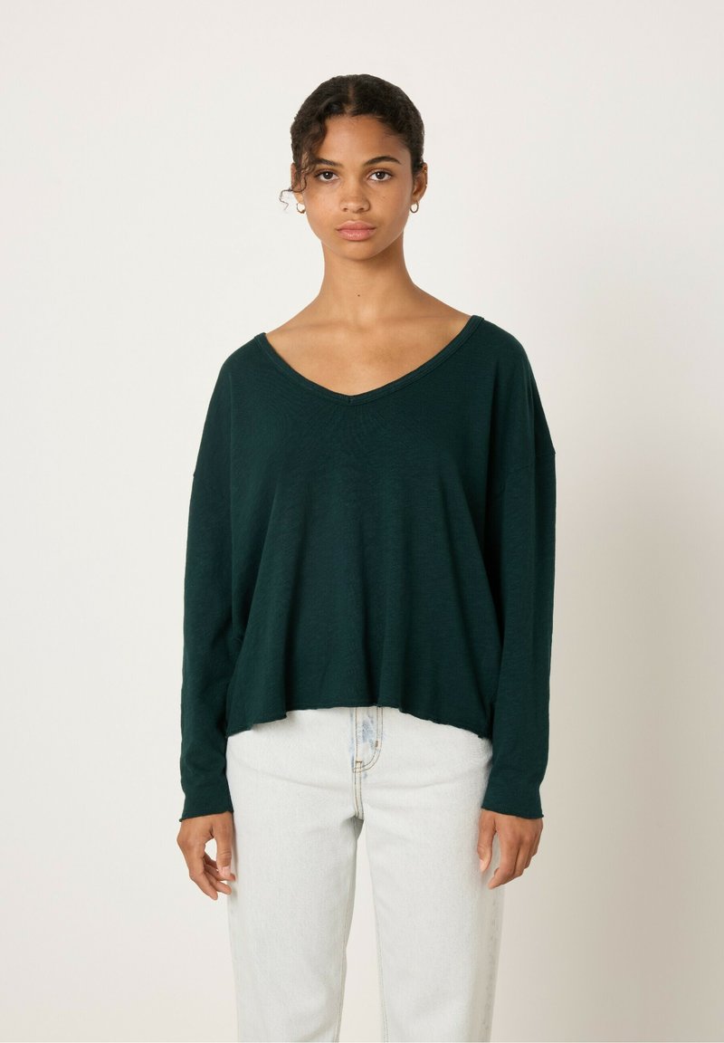 Tumši zaļa, brīvi pieguļoša, garām piedurknēm ar plašu V formu izgriezumu. Viegls audums un brīvi iekārtota apakšmala lieliski saskan ar gaišas krāsas džinsiem.