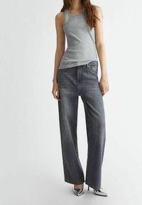 Grijze tanktop met een ronde halslijn, gecombineerd met wijde denim jeans in een donkere kleur. De outfit wordt aangevuld met zilveren puntige hakken.