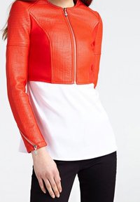 Rood en witte cropped jasje met een textuur, gewatteerd ontwerp en ritssluiting. Heeft lange mouwen met zilveren ritssluiting accenten.