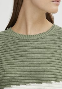 Pull en laine vert tricoté avec un motif texturé en côtes. Encolure ronde et légère usure au niveau de l'ourlet. Apparence de tissu doux.