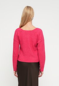 Różowy prążkowany sweter z długimi rękawami i szerokim dekoltem, o krótkim kroju, zestawiony z brązową spódnicą.