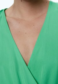 Vêtement vert en V, fabriqué en tissu lisse, présentant un design enroulé et un minimum de couture le long des bords.