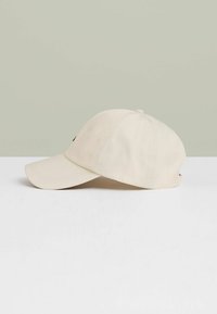 Beige baseballkasket med en buet skygge, letvægtsstof, syninger og et lille logo på det venstre forreste panel.