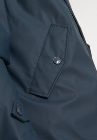 Tmavě modrá voděodolná bunda s šikmou kapsou a uzávěrem na patentku a hladkou, matnou texturou.