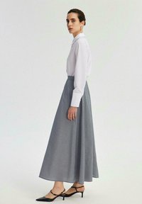 Bela srajca z gumbi, v kombinaciji z dolgim, vzorčastim modrim in belim krilom. Obleka vključuje tanke črne pete in elegantno silhueto.