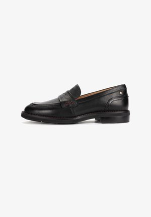 Mocassin penny en cuir noir avec talon bas, bout mocassin, surpiqûres décoratives et petit clou métallique à l'arrière.