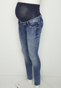 Jeans de maternidad en denim azul desgastado con una cinturilla negra elástica. Presenta un ajuste ajustado y acentos desgastados en las piernas.