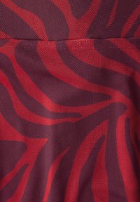 Detail červené a tmavě fialové látky s abstraktními pruhy připomínajícími zebru a viditelnou tkanou texturou.