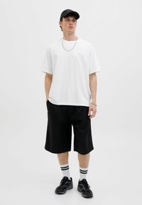 Hvid bomulds t-shirt, sorte knæ-lange shorts, sort kasket og sorte sneakers med hvide stribede strømper; enkelt design, afslappet pasform.