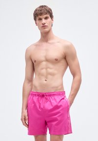 Φουξ ρόζ μαγιό βερμούδα με ελαστική μέση, κορδόνι και πλαϊνές τσέπες. Διαθέτει λογότυπο στη ραφή. Ομαλή υφή.
