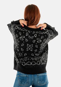 Zwarte wollen trui met witte bloemenpatronen, een losse pasvorm, brede halslijn en lange mouwen, gecombineerd met blauwe denim jeans.