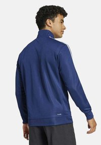 Giacca sportiva blu navy con colletto alto, maniche lunghe e strisce laterali bianche, realizzata in tessuto liscio, con una silhouette aderente.