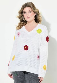 Maglione bianco lavorato a maglia con scollatura a V, decorato con applicazioni floreali colorate in rosso, rosa, giallo e verde. Dettaglio di filato testurizzato.