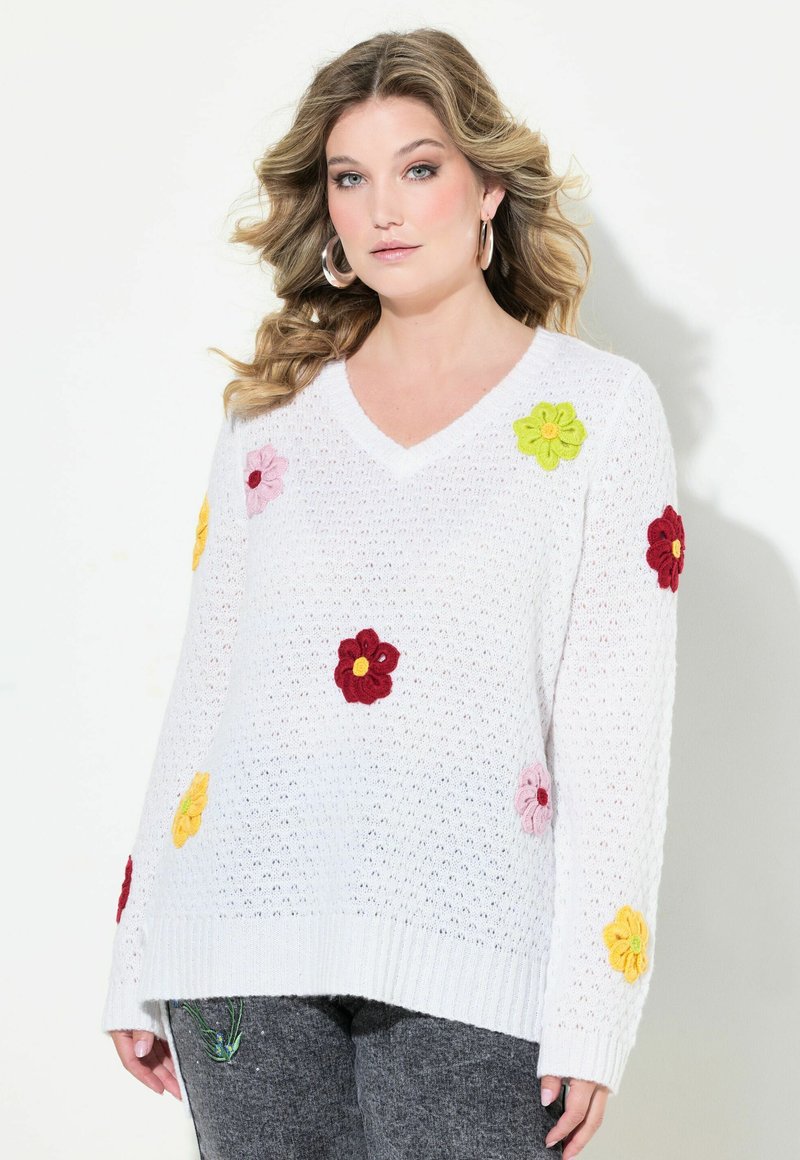Maglione bianco lavorato a maglia con scollatura a V, decorato con applicazioni floreali colorate in rosso, rosa, giallo e verde. Dettaglio di filato testurizzato.