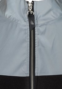 Veste zippée grise et noire avec un détail de zip argenté, matériau supérieur lisse et section inférieure en polaire texturée.