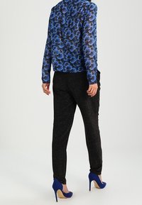 Blå blommig blus med långa ärmar, matchad med svarta glittriga byxor och blå högklackade skor, sedd bakifrån.