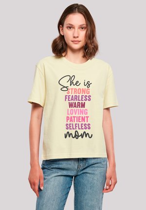 Light yellow cotton T-shirt featuring multicolored text: "She is STRONG, FEARLESS, WARM, LOVING, PATIENT, SELFLESS, mom" in various fonts.