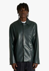 Giacca in finta pelle verde con colletto, chiusura con bottoni e maniche lunghe. Texture opaca, design minimalista, adatta a vari stili.