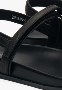 Zwarte sandalen met platte zolen, voorzien van twee slanke leren banden die bovenaan kruisen. De inlegzool heeft een matte textuur en een subtiele glans.