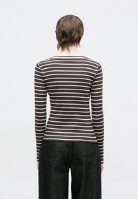 Pika varrukaga pluus tumedates pruunides ja valgetes horisontaalsetes triipudes, liibuv disain, sooniline tekstuur. Ühendatud tumeda teksapükstega.