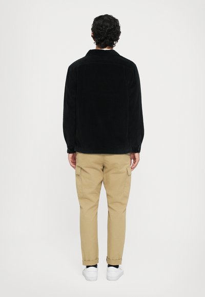 Black corduroy jacket with a relaxed fit, featuring long sleeves and a collar. Paired with khaki cargo pants and white sneakers.