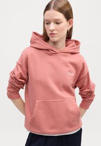 Ružová mikina s kapucňou vyrobená z mäkkej tkaniny, so zapínaním vpredu a obratými manžetami. Jemný logotyp na hrudi.
